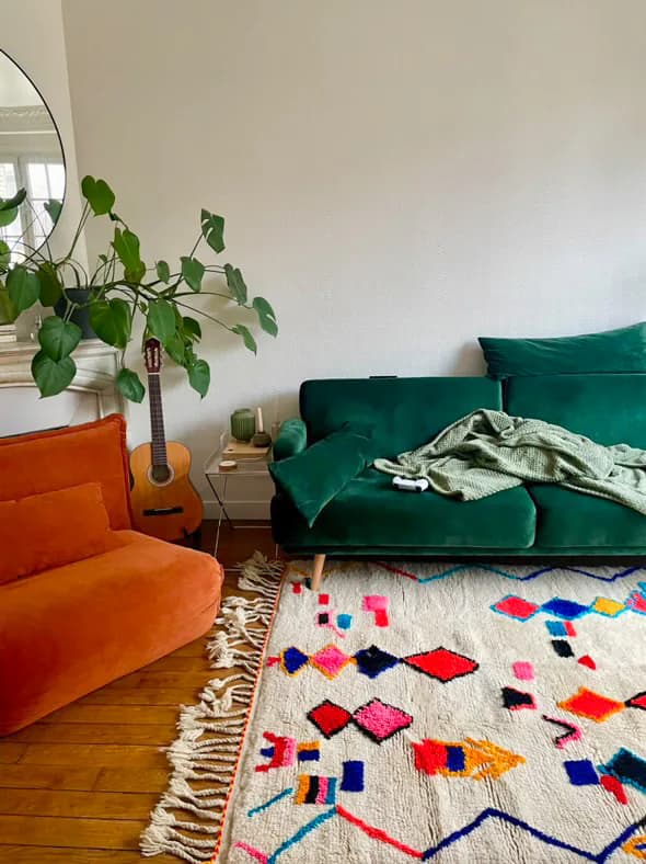 Tapis berbère multicolore entre un canapé vert et un fauteuil orange