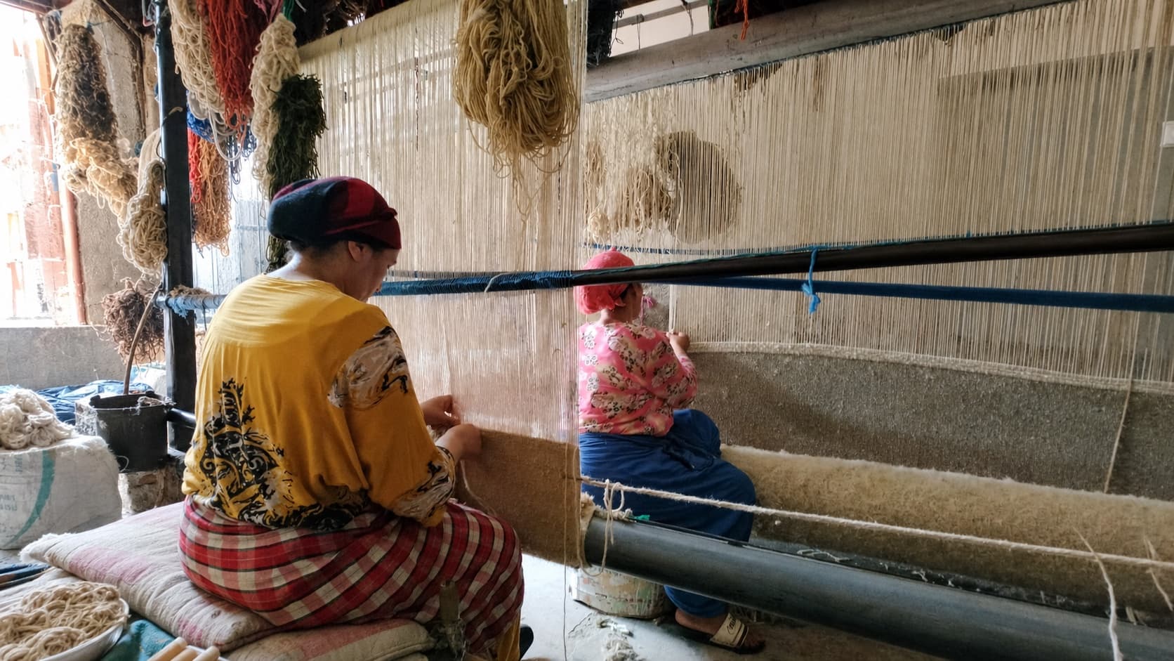 Deux artisanes tissent un tapis à la main sur un métier traditionnel au Maroc